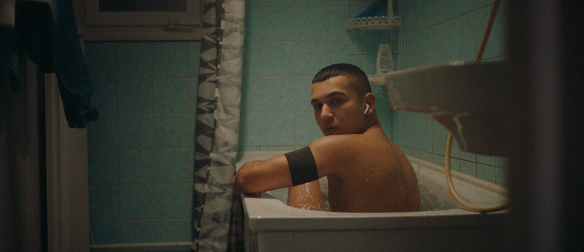 Eine Person mit kurzen Haaren sitzt in der Badewanne und dreht sich zur Kamera.