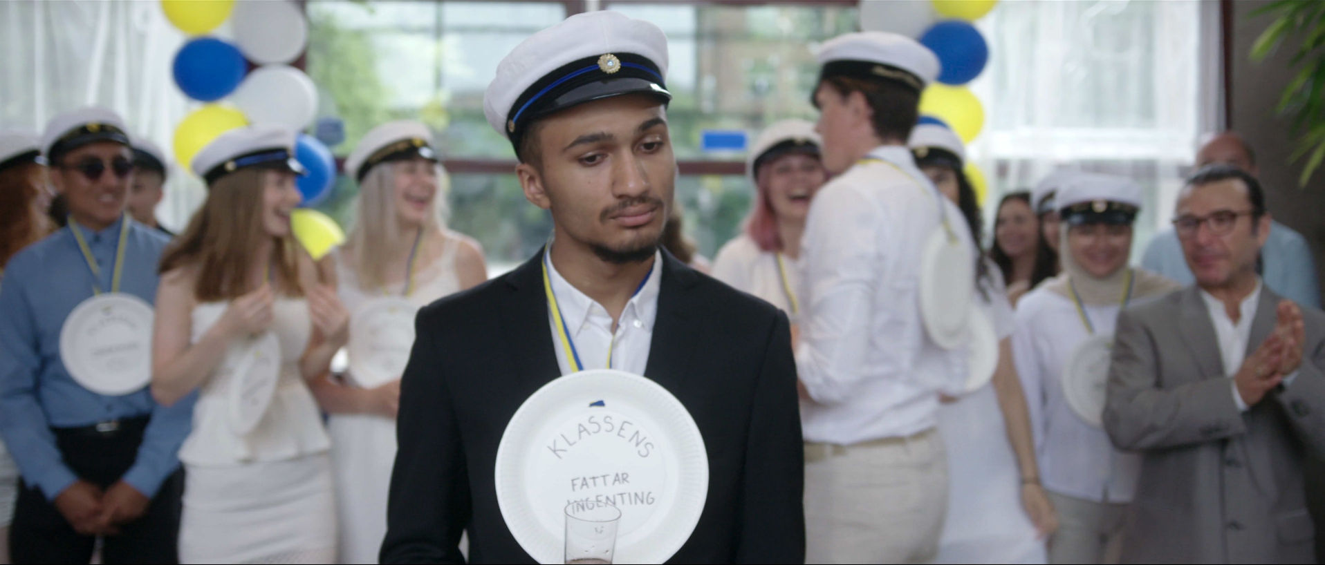 Eine Person in Uniform mit einer Medaille um den Hals. Im Hintergrund eine Party.