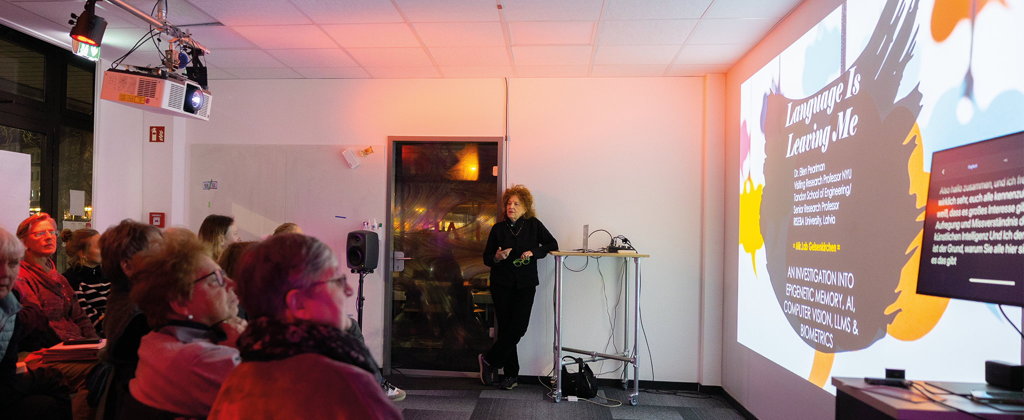 Dr. Ellen Pearlman hält einen Vortrag mit einer Projektion vor mehreren sitzenden Menschen