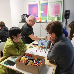 Im Bild sitzen Personen um einen Tisch herum und bauen mit Lego.