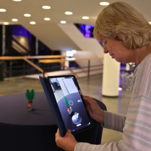 Frau hält Ipad in der Hand und führt einen 3D Scan durch mit einer Legofigur.