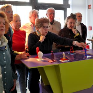 Ältere Menschen stehen um ein Spielfeld und testen die Spielfiguren.