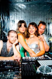 Die Band "Vitamin Dream" posiert in schillernden Kostümen hinter ihrem Turntable