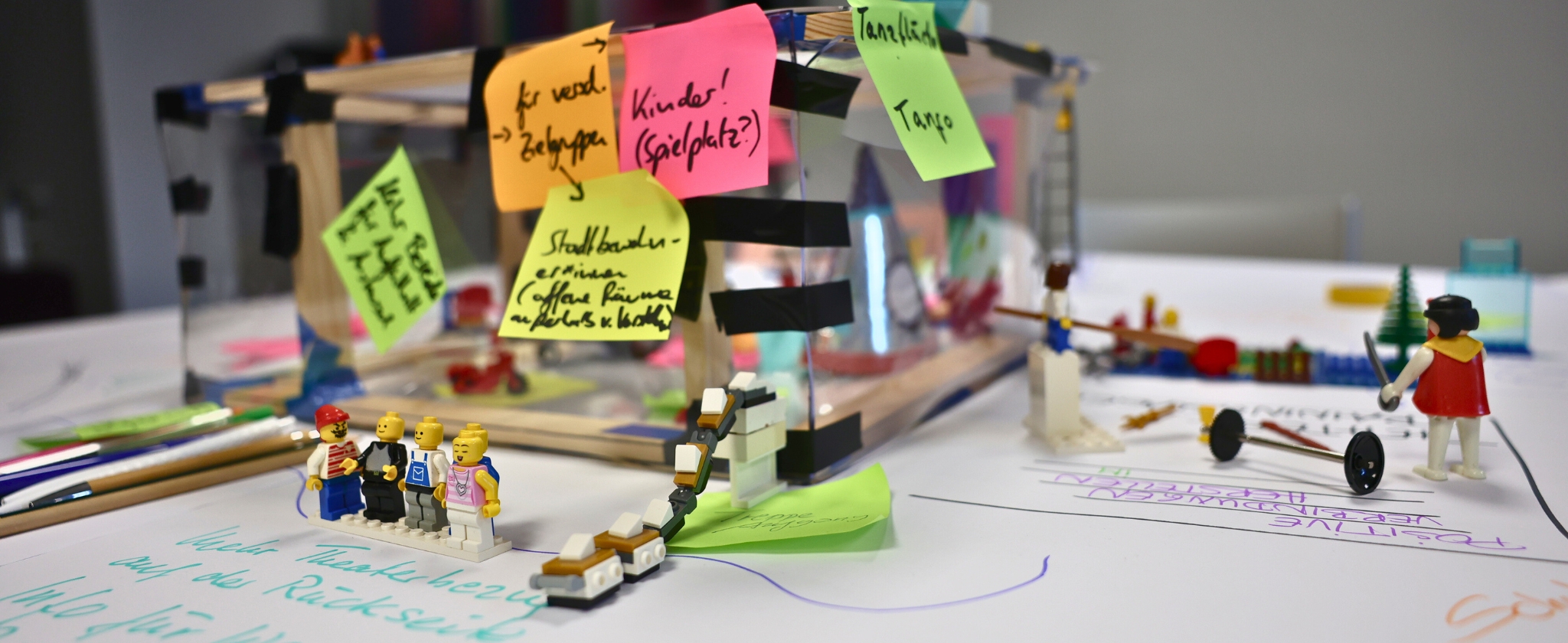 In der Mitte vom Foto ist ein Gebautes Theater aus Holz und Folie zu sehen mit vielen Bunten Zetteln dran. Vorne Links und Rechts im Bild stehen Lego Figuren und Gegenstände.
